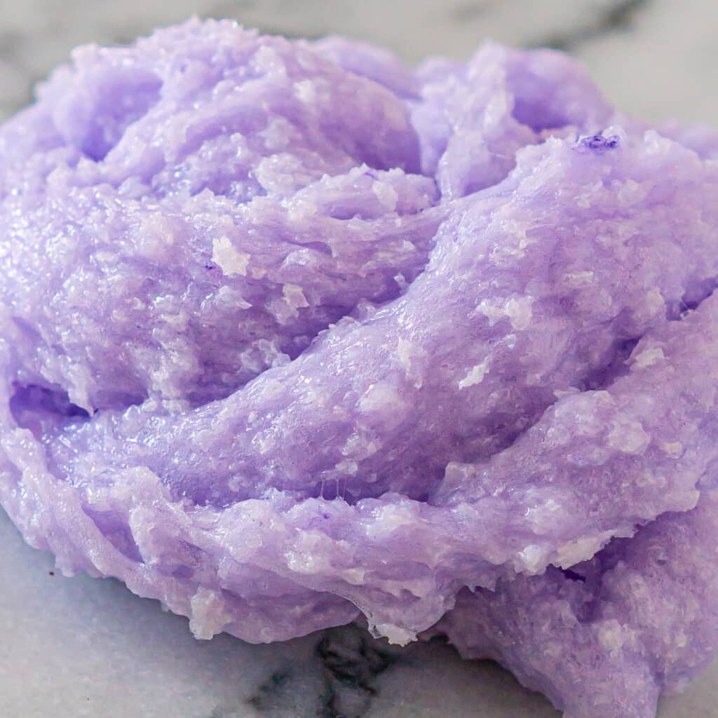 Closeup of a clear lilac slime filled with tiny bits of shredded hard plastic to make a snow fizz slime texture.