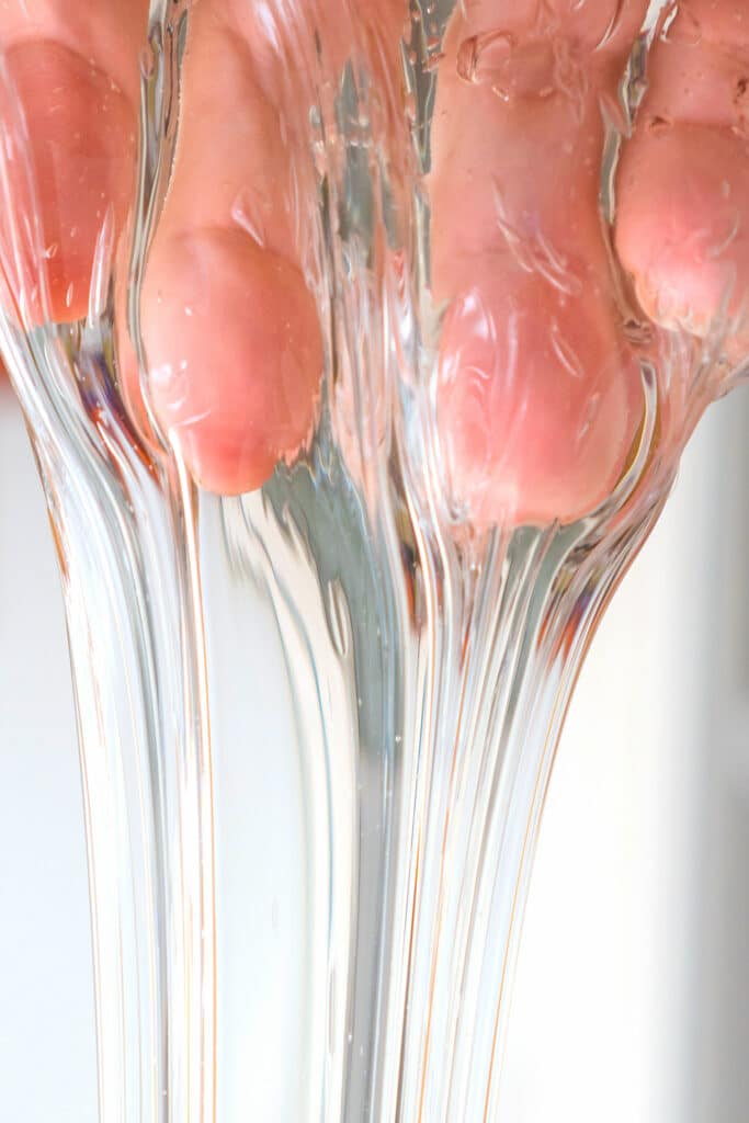 Extreme closeup of completely transparent clear slime flowing over four fingertips and down into a stream like a waterfall in front of a white background.