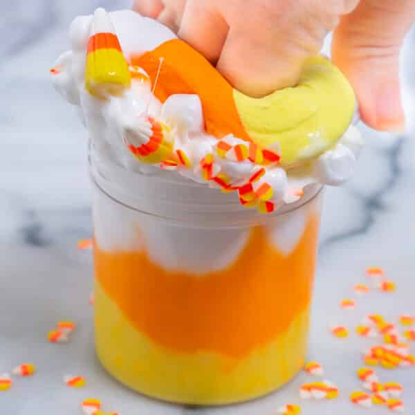 A giant clay candy corn is getting squished down into a jar of white, orange, and yellow glossy slime.