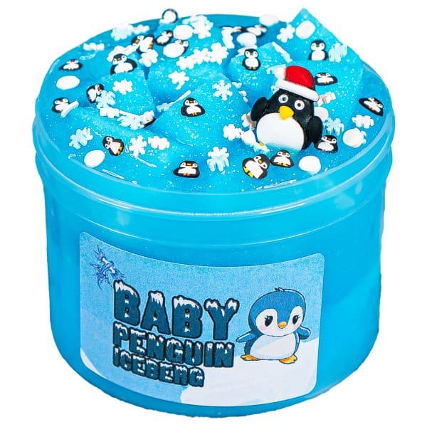 A clear jar is overfilled with a bright, shimmery, light turquoise jelly slime. The slime is piled up high above the top of the jar with white foam jelly cubes mixed in and resting on top like icebergs. Fake sprinkles shaped like penguins and snowflakes are sprinkled on top, and a charm of a penguin wearing a Santa hat is nestled into the slime. A label on the jar reads Baby Penguin Iceberg Slime