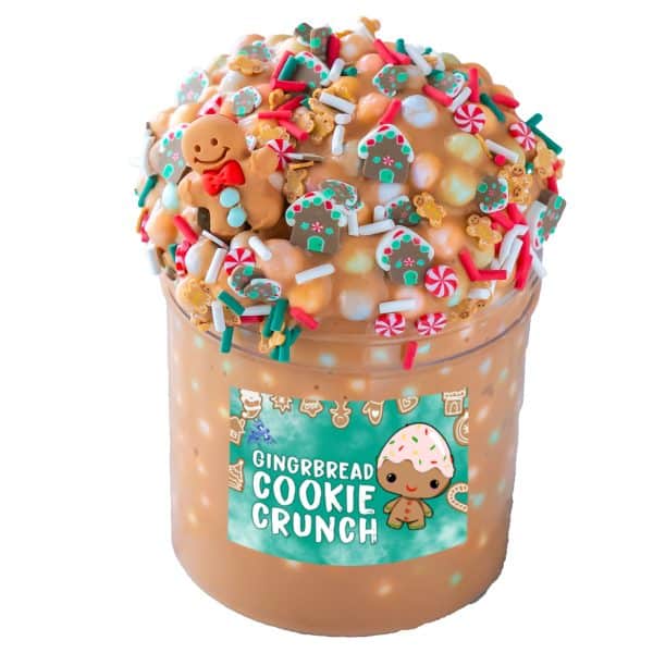 A clear jar is filled with a glossy light brown slime packed with multicolor pastel foam beads. The slime is mounded high above the top of the jar and covered in a gingerbread house sprinkle mix. A small gingerbread man charm is nestled into the top pile of gingerbread floam slime, and a label on the jar reads Gingerbread Cookie Crunch.