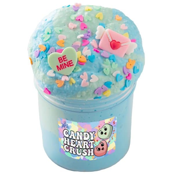 A clear jar is packed with pastel green and blue slime, piled high above the rim. The slime texture is bumpy from bits of tiny plastic snow, and the mound of slime is topped with fake multicolor heart sprinkles, a fake conversation heart candy, and a pink Valentine's card charm. A lable on the jar reads Candy Heart Crush slime.