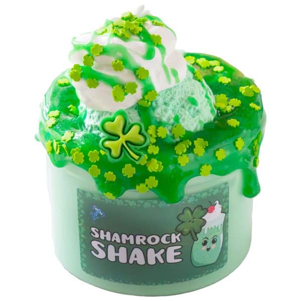 A translucent jar is filled with a pale green slime, and has a bright green clear slime spreading and dripping over the top. On top of that is mint green clay that looks like a scoop of ice cream. The clay is topped with a swirl of white butter slime to resemble whipped cream, drizzled with more green syrup slime, and sprinkled with shamrock sprinkles and a shamrock charm. A label reads Shamrock Shake Slime.