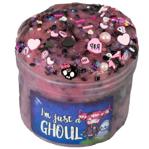 A jar is filled with shimmery rose pink clear slime, that’s with black bingsu beads and topped with a mix of pink and black sprinkles that blend both creepy and girly vibes, like skulls, hearts, and tombstones. The jar's label reads "I'm Just a Ghoul" with a cute, spooky illustration of a character with pigtails and a mischievous expression.